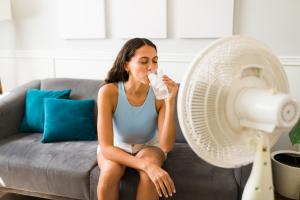 Une femme boit un verre d'eau frais devant un ventilateur