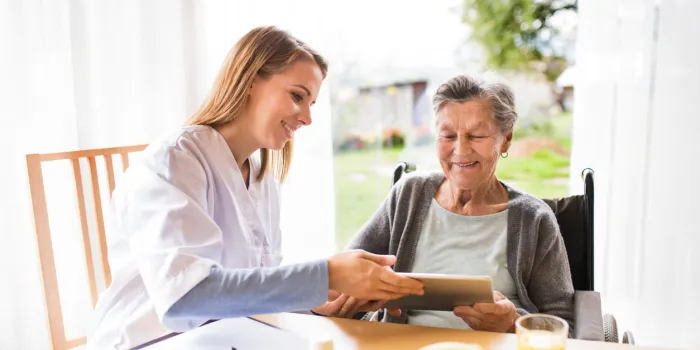 health visitor and a senior woman with tablet during home visit a nurse talking to an elderly woman