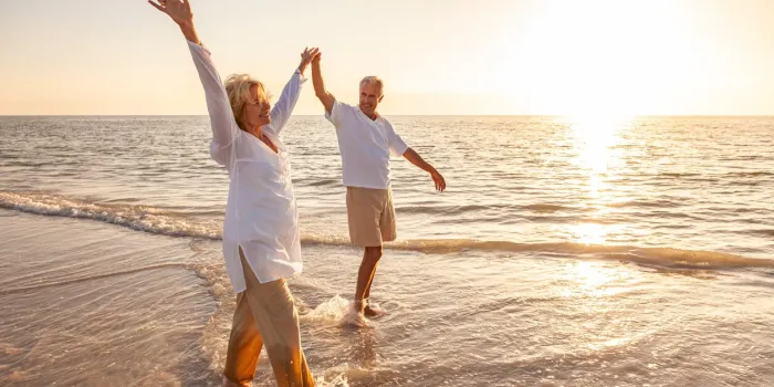 happy senior man and woman old retired couple walking and holding hands on a beach at sunset happy senior man and woman old retired couple walking and holding hands on a beach at sunset