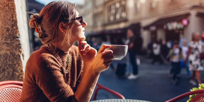 portrait of fashionable stylish woman relaxing in outdoor cafe drinking coffee woman enjoying architecture of lviv city sitting at table on street alone