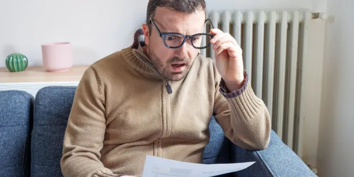 shocked man reading some bills energy expenses on sofa living room